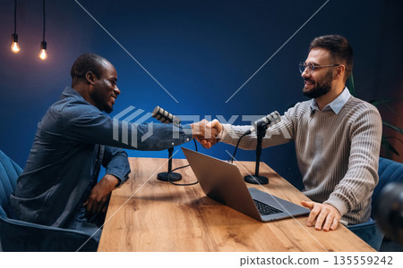 Greetings gesture. Two radio presenters recording an audio broadcast in a studio Greetings gesture. Two radio presenters recording an audio broadcast in a studio 135559242