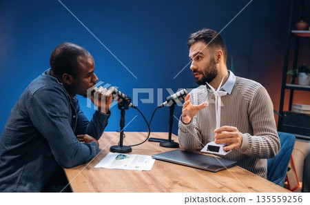 Active communication. Two radio presenters recording an audio broadcast in a studio Active communication. Two radio presenters recording an audio broadcast in a studio 135559256