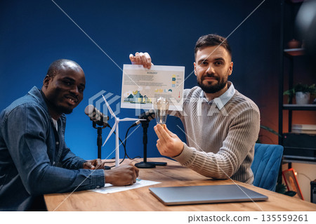 Ecology conception, with paper. Two radio presenters recording an audio broadcast in a studio Ecology conception, with paper. Two radio presenters recording an audio broadcast in a studio 135559261
