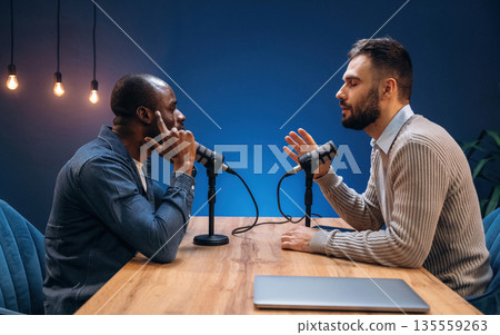 Two radio presenters recording an audio broadcast in a studio 135559263