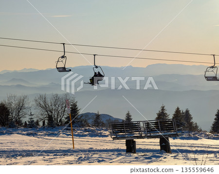Chairlift silhouettes against layered mountain horizon during sunset in Kopaonik. Atmospheric travel mood, winter calm, and scenic elevation through light, distance, and alpine tranquility. Chairlift silhouettes against layered mountain horizon during sunset in Kopaonik. Atmospheric travel mood, winter calm, and scenic elevation through light, distance, and alpine tranquility. 135559646