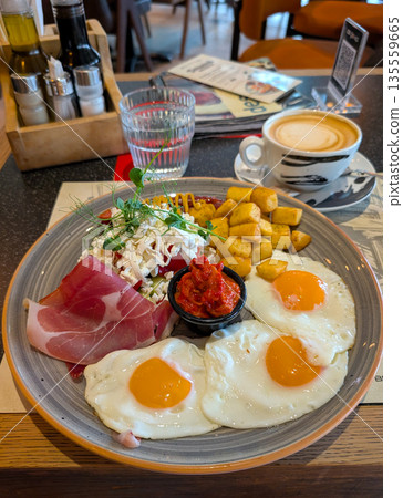 Hearty breakfast plate with eggs ham cheese and vegetables in cafe. Balanced meal choice, social dining, and modern breakfast culture in casual restaurant setting. 135559665
