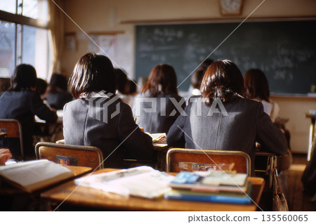 一張充滿懷舊氣息的日本學校背影照，展現了黃昏時分一位女學生在教室裡學習的場景。 135560065