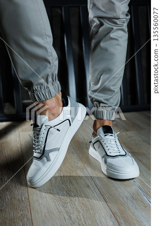 Male legs in white leather summer shoes. Comfortable men's white sneakers with laces. Casual men's sneakers Male legs in white leather summer shoes. Comfortable men's white sneakers with laces. Casual men's sneakers 135560077