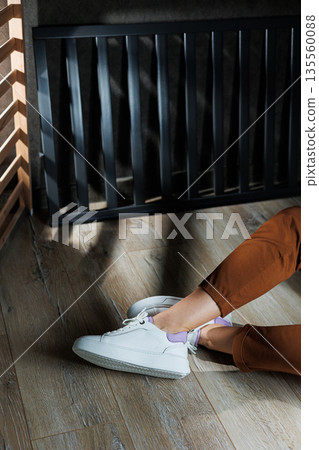 White leather sneakers on women's legs. Women's legs in comfortable casual sneakers 135560088