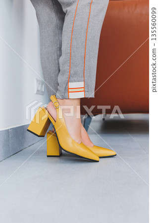 A slender woman sits in a chair in high-heeled sandals. Collection of summer women's shoes 135560099