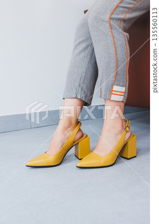 A slender woman sits in a chair in high-heeled sandals. Collection of summer women's shoes 135560113