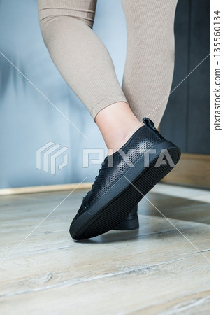 Collection of women's shoes. Black leather sneakers on women's feet. Female feet in comfortable casual sandals 135560134