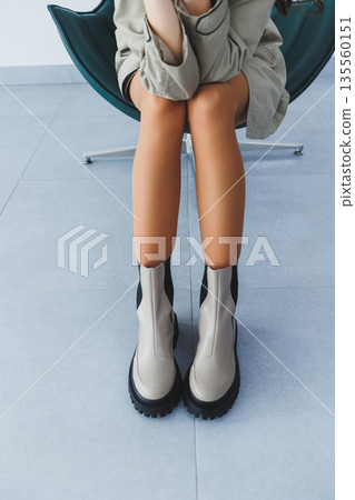 Beautiful brunette woman in an autumn trench coat and leather boots posing in the studio. Women's fashion 135560151