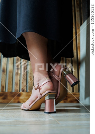Fragile female legs in beige leather sandals. Collection of summer women's shoes. Stylish women's shoes for the summer. Women's sandals on women's feet 135560158