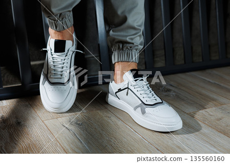 Casual white sneakers for men. Male legs in white leather summer shoes. Comfortable men's white sneakers with laces. 135560160
