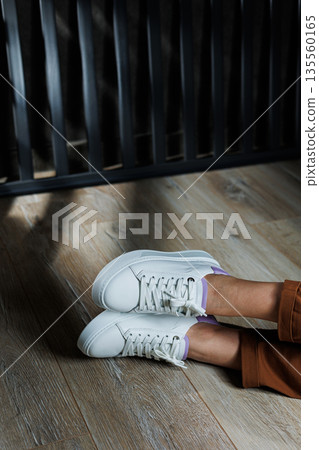 Comfortable female legs in white sneakers with flat soles. Close-up of female legs in leather sneakers. Women's summer sneakers. Collection of women's leather shoes Comfortable female legs in white sneakers with flat soles. Close-up of female legs in leather sneakers. Women's summer sneakers. Collection of women's leather shoes 135560165