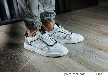 Male legs in white leather summer shoes. Comfortable men's white sneakers with laces. Casual men's sneakers 135560239