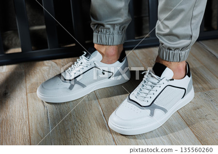 Casual white sneakers for men. Male legs in white leather summer shoes. Comfortable men's white sneakers with laces. 135560260