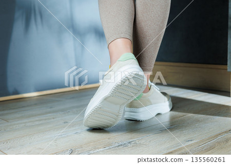 Close-up of female legs in leather sneakers on feet. Modern seasonal collection of stylish sneakers. Women's fashion. Close-up of female legs in leather sneakers on feet. Modern seasonal collection of stylish sneakers. Women's fashion. 135560261