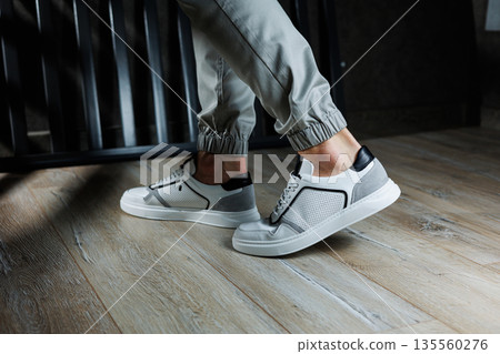 Male legs in white leather summer shoes. Comfortable men's white sneakers with laces. Casual men's sneakers Male legs in white leather summer shoes. Comfortable men's white sneakers with laces. Casual men's sneakers 135560276