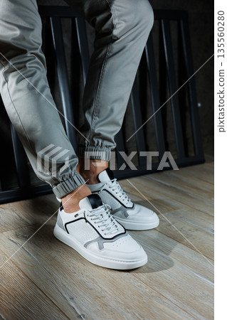 Male legs in white leather summer shoes. Comfortable men's white sneakers with laces. Casual men's sneakers Male legs in white leather summer shoes. Comfortable men's white sneakers with laces. Casual men's sneakers 135560280
