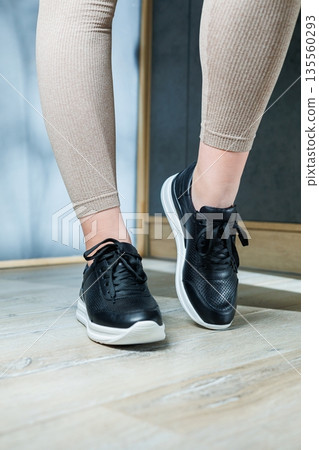 Collection of women's shoes. Black leather sneakers on women's feet. Female feet in comfortable casual sandals 135560293