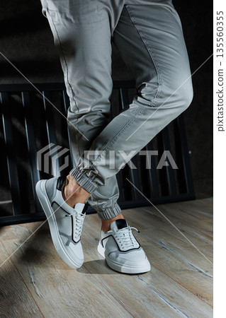 Male legs in white leather summer shoes. Comfortable men's white sneakers with laces. Casual men's sneakers Male legs in white leather summer shoes. Comfortable men's white sneakers with laces. Casual men's sneakers 135560355