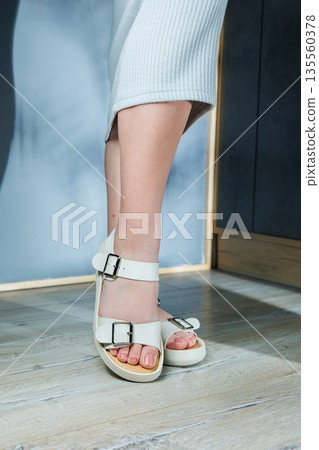 White leather sandals on women's feet. Female feet in comfortable casual sandals 135560378
