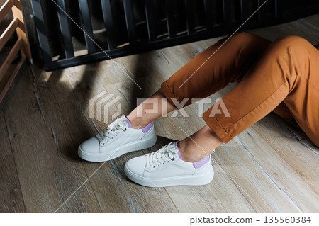 White leather sneakers on women's legs. Women's legs in comfortable casual sneakers 135560384