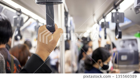 A male passenger's hand grips a subway pole amidst a crowded urban commute, a classic city life scene 135560389
