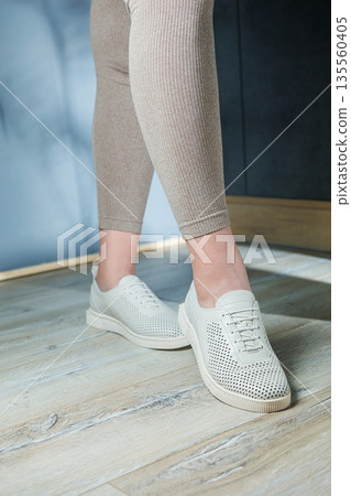 Female legs in white casual sneakers. Comfortable women's summer shoes. Female legs in white casual sneakers. Comfortable women's summer shoes. 135560405
