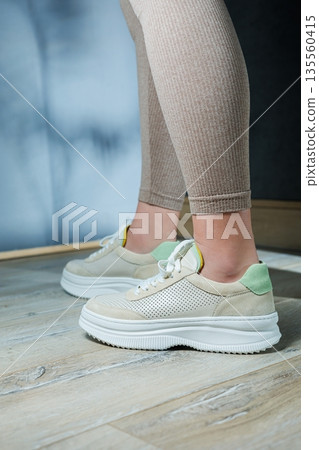 Close-up of female legs in leather sneakers on feet. Modern seasonal collection of stylish sneakers. Women's fashion. Close-up of female legs in leather sneakers on feet. Modern seasonal collection of stylish sneakers. Women's fashion. 135560415