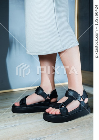 Black sports women's sandals on the feet. Stylish women's shoes for the summer. Collection of summer women's shoes. Black sports women's sandals on the feet. Stylish women's shoes for the summer. Collection of summer women's shoes. 135560424