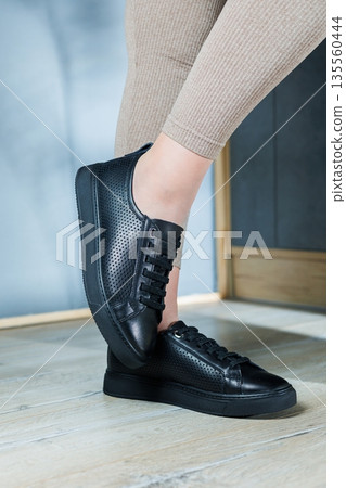 Collection of women's shoes. Black leather sneakers on women's feet. Female feet in comfortable casual sandals 135560444