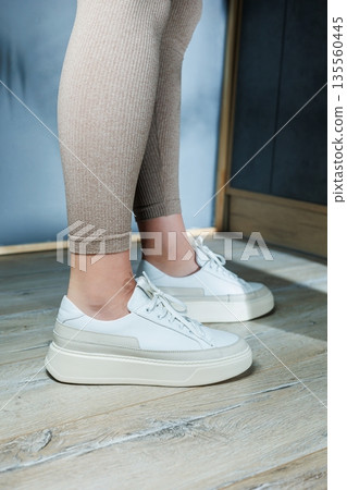 White leather women's classic sneakers on the feet. Stylish women's shoes for the summer. Collection of summer women's shoes. 135560445