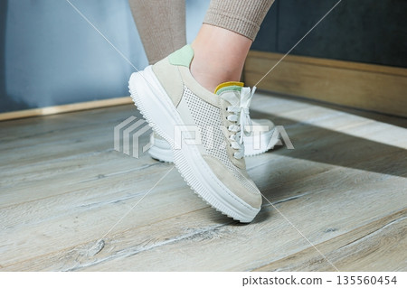 Close-up of female legs in leather sneakers on feet. Modern seasonal collection of stylish sneakers. Women's fashion. Close-up of female legs in leather sneakers on feet. Modern seasonal collection of stylish sneakers. Women's fashion. 135560454