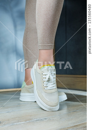 Close-up of female legs in leather sneakers on feet. Modern seasonal collection of stylish sneakers. Women's fashion. Close-up of female legs in leather sneakers on feet. Modern seasonal collection of stylish sneakers. Women's fashion. 135560480