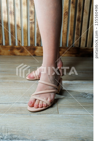 Female legs in summer beige flip flops. Women's summer shoes. Women's leather flip flops. Female legs in summer beige flip flops. Women's summer shoes. Women's leather flip flops. 135560496