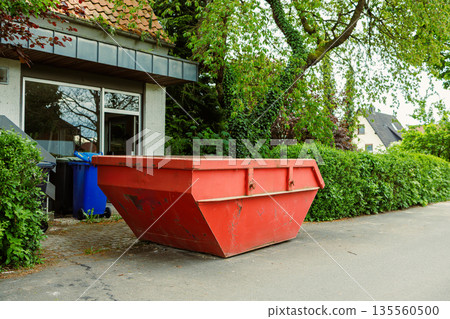 Large street garbage container. Metal red container for construction waste. Garbage container standing near the house during renovation. 135560500