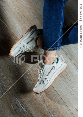 Female legs in white casual sneakers. Comfortable sports women's summer shoes. 135560503