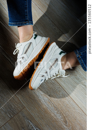 Female legs in white casual sneakers. Comfortable sports women's summer shoes. Female legs in white casual sneakers. Comfortable sports women's summer shoes. 135560512