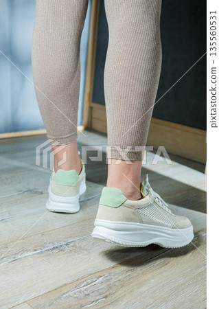 Close-up of female legs in leather sneakers on feet. Modern seasonal collection of stylish sneakers. Women's fashion. Close-up of female legs in leather sneakers on feet. Modern seasonal collection of stylish sneakers. Women's fashion. 135560531
