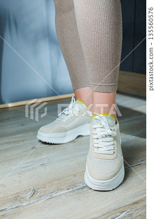 Close-up of female legs in leather sneakers on feet. Modern seasonal collection of stylish sneakers. Women's fashion. Close-up of female legs in leather sneakers on feet. Modern seasonal collection of stylish sneakers. Women's fashion. 135560576