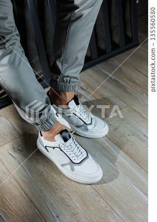 Male legs in white leather summer shoes. Comfortable men's white sneakers with laces. Casual men's sneakers Male legs in white leather summer shoes. Comfortable men's white sneakers with laces. Casual men's sneakers 135560580