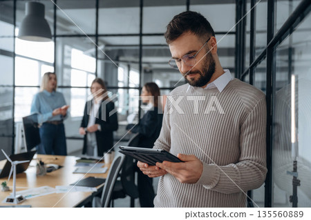 Guy in glasses is standing. Business people are working in the office 135560889