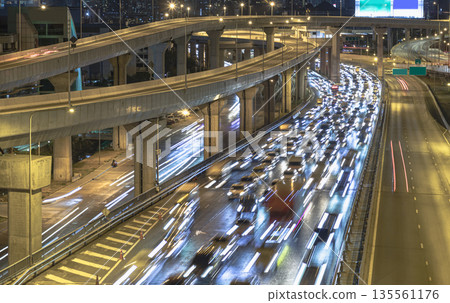 A nightscape view with bright glowing light trails effect of many cars headlights and rear lights on urban expressway. 135561176