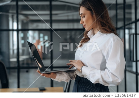 With a laptop. Beautiful woman is in the office 135561437