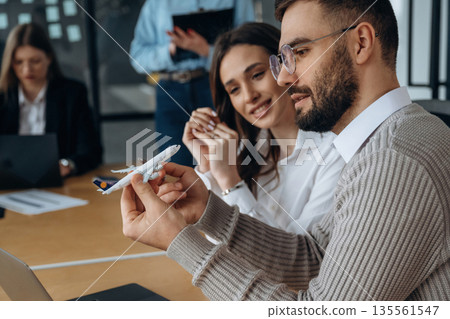 Small toy plane in hands. Business people are working in the office 135561547