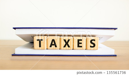 Taxes symbol. Concept word Taxes on beautiful wooden blocks in book. Beautiful wooden table white background. Business lifestyle taxes concept. Copy space. Taxes symbol. Concept word Taxes on beautiful wooden blocks in book. Beautiful wooden table white background. Business lifestyle taxes concept. Copy space. 135561736
