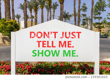 Tell or show symbol. Concept words Do not just tell me, show me on beautiful white road sign. Beautiful palm trees blue sky background. Business tell or show concept. Copy space. Tell or show symbol. Concept words Do not just tell me, show me on beautiful white road sign. Beautiful palm trees blue sky background. Business tell or show concept. Copy space. 135561810