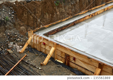 A concrete foundation is being poured on the construction site. Wooden formwork is used.  135561869