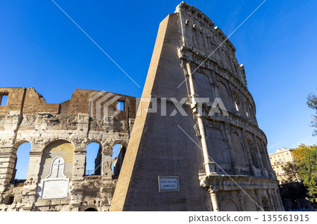 Famous Coliseum in Rome. Colosseum, or Coliseum. Part of the wall of an antique stone structure with arches. Italy, Europe. Famous touristic place in the world, Europe. Beautiful blue sky background. 135561915