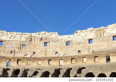 Famous Coliseum in Rome. Colosseum, or Coliseum. Part of the wall of an antique stone structure with arches. Italy, Europe. Famous touristic place in the world, Europe. Beautiful blue sky background. Famous Coliseum in Rome. Colosseum, or Coliseum. Part of the wall of an antique stone structure with arches. Italy, Europe. Famous touristic place in the world, Europe. Beautiful blue sky background. 135561916