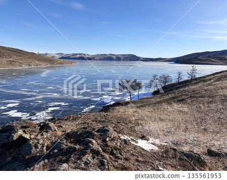 Frozen Lake Baikal. View of clear ice, snow-capped mountains. Frozen Lake Baikal. View of clear ice, snow-capped mountains. 135561953